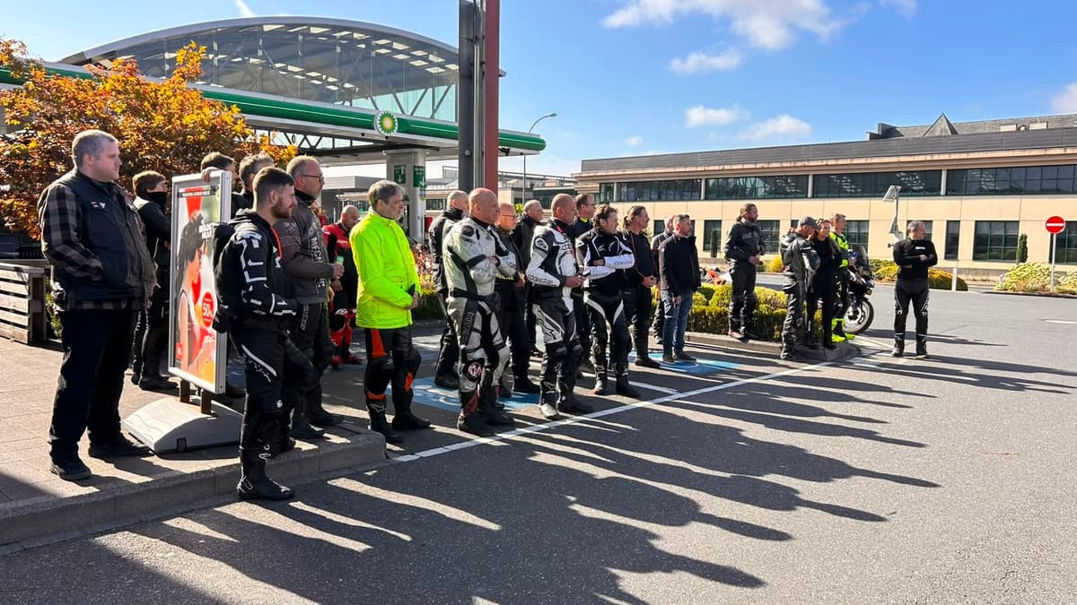 Een rij motorrijders in leren pakken luistert naar de briefing op de parking van het BP-tankstation in Wemperhardt, met lange schaduwen in de ochtendzon.