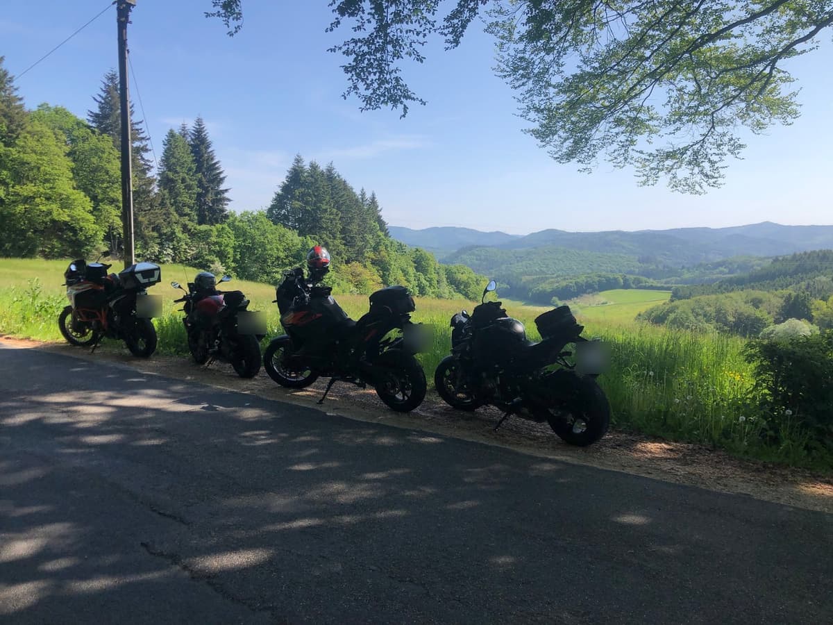 Vier motoren in de berm van een landweg in de zon, met een weids uitzicht over de beboste heuvels van de Eifel.