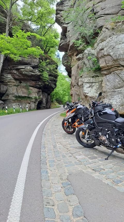 Twee motoren op de stoeprand van een bochtig baantje tussen hoge zandsteenrotsen en fris groen.
