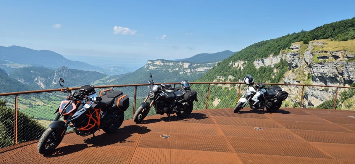 Drie motoren staan op een stalen uitkijkplatform boven een groen dal met kalkrotsen.