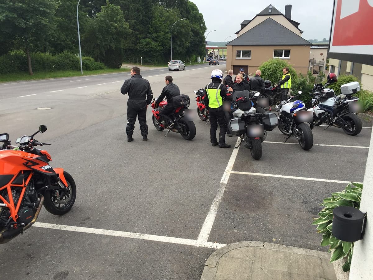 Motorrijders met fluohesjes lopen tussen hun geparkeerde motoren op de parking van een tankstation, klaar om te vertrekken.