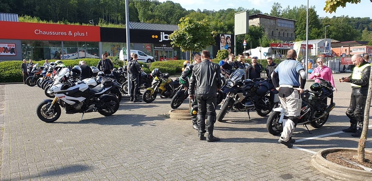 Motorrijders in leren pakken staan tussen hun geparkeerde motoren, met vooraan een zwarte BMW en een zwart-witte sportmotor.