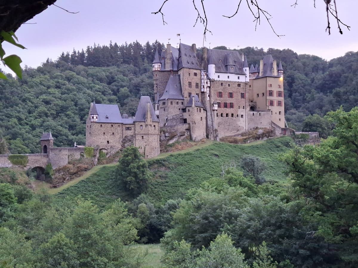 Burg Eltz, een kasteel met torentjes en vakwerk op een rots tussen beboste hellingen, in de avondschemering.