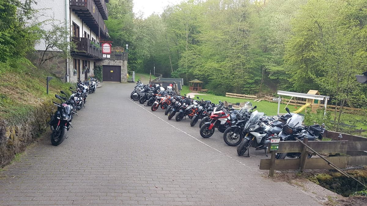 Een lange rij motoren op de oprit van een hotel met houten balkons, in een groen, bebost dal.