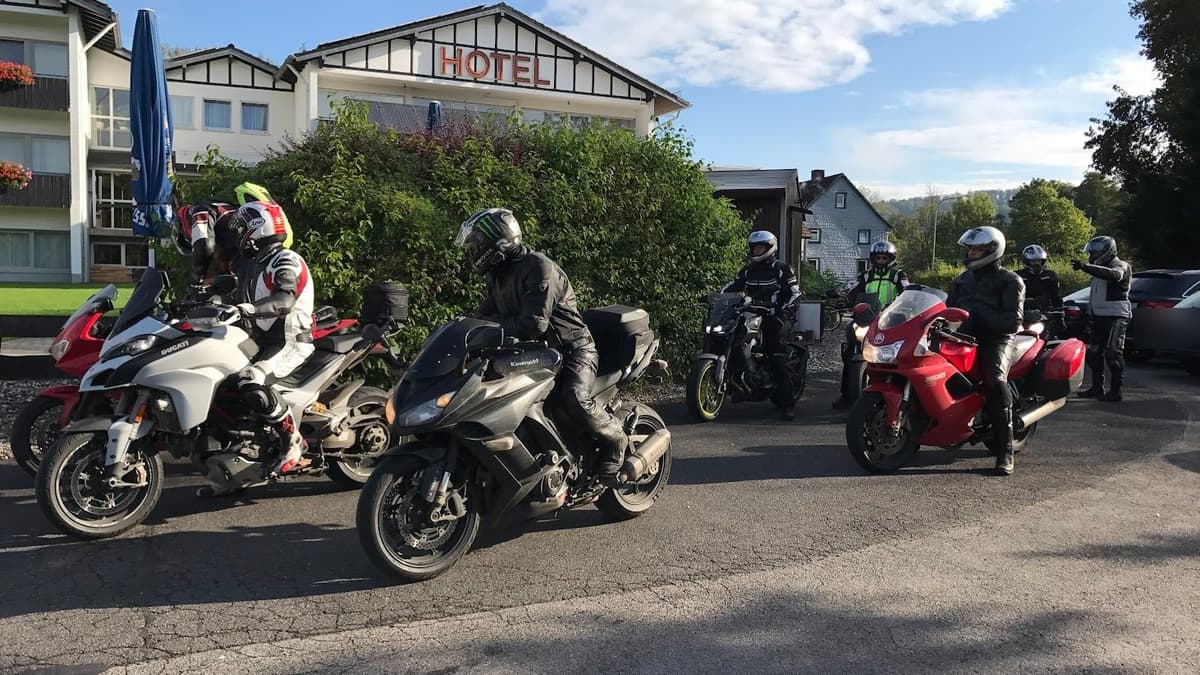 Motorrijders met helm op vertrekken op hun motoren van de parking van een hotel, in de ochtendzon.