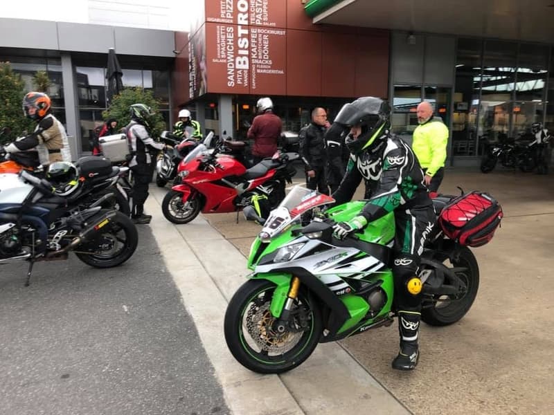 Een motorrijder in een zwart, wit en groen pak op een groene Kawasaki, tussen andere motorrijders aan een tankstation.