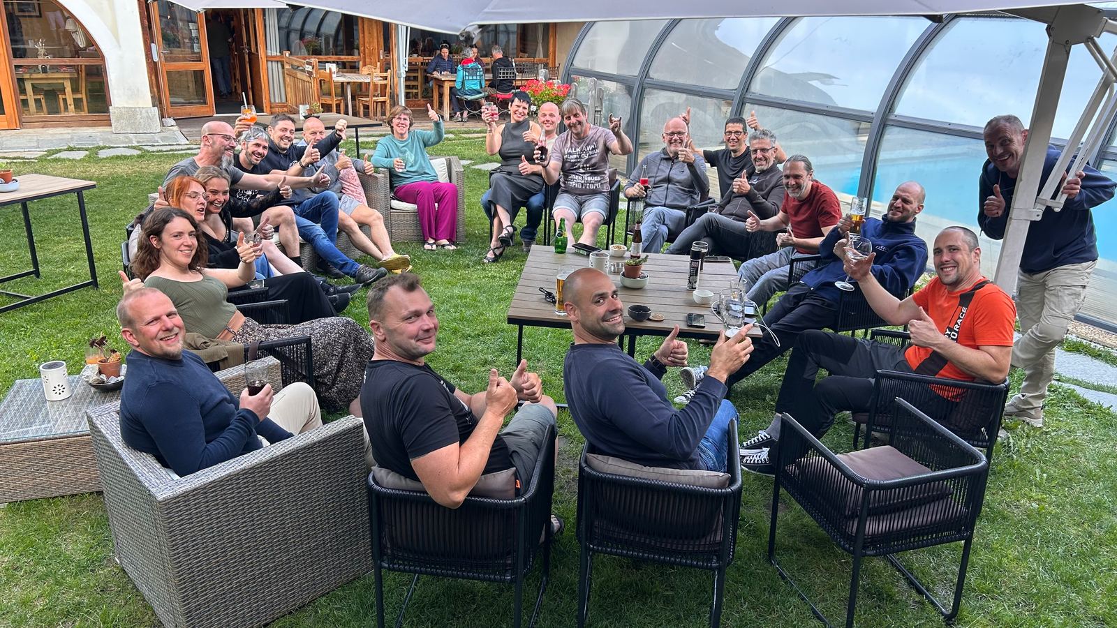 Een groep zit in een tuin op loungestoelen en steekt de duimen omhoog naar de camera.