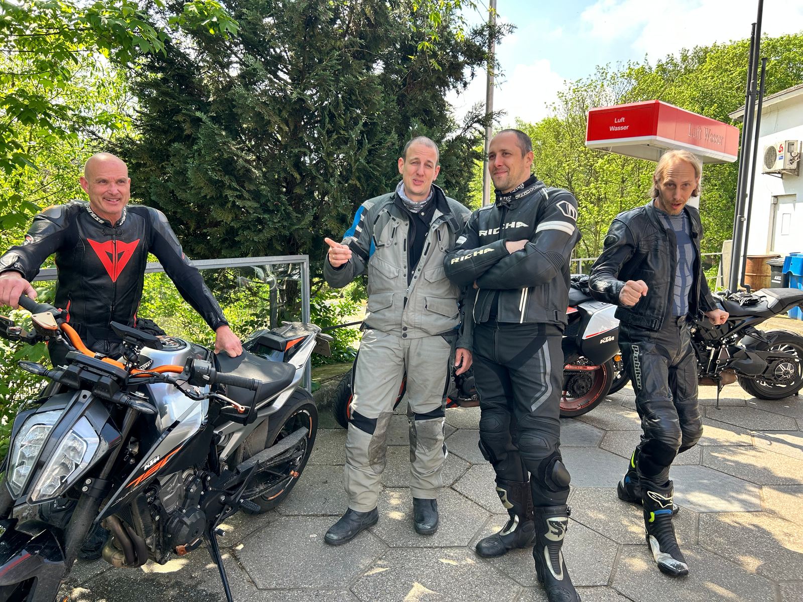 Vier motorrijders in motorpak staan lachend bij hun motoren tijdens een stop.