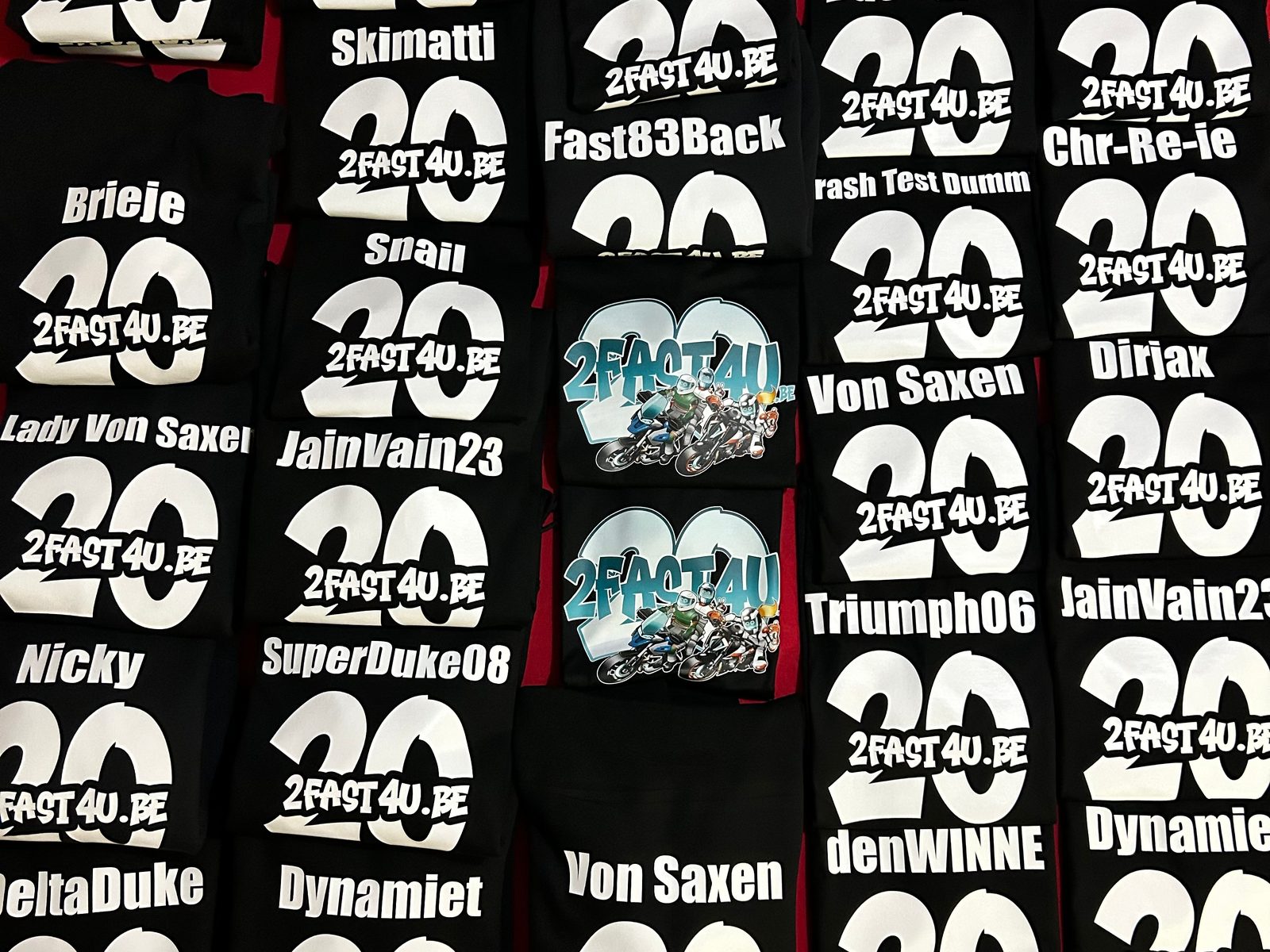 Zwarte 2fast4u-hoodies voor 20 jaar 2fast4u naast elkaar, de meeste met een nickname en een grote 20 op de rug, twee met het blauwe 20-jaarlogo met motorrijders.