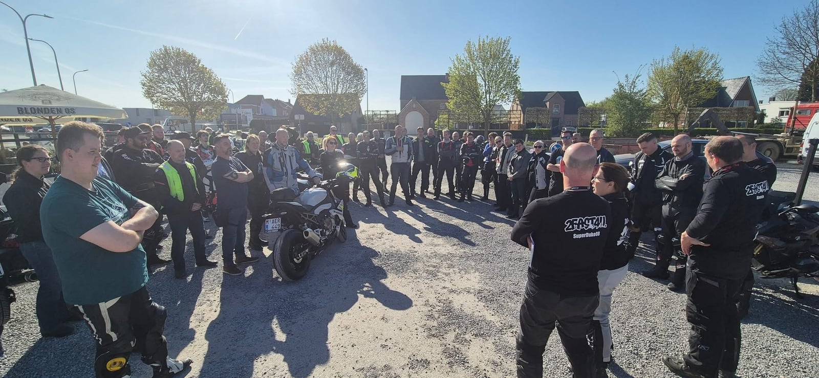 Een grote groep motorrijders staat in een kring tussen de motoren.